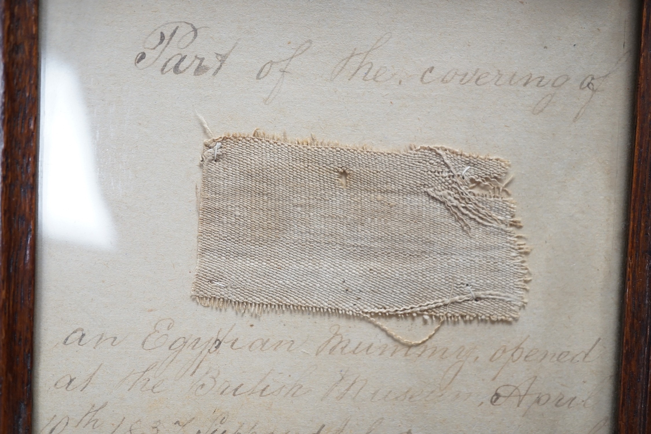 A small 19th century framed textile fragment, mounted with handwritten script; “part of the covering of an Egyptian Mummy opened at the British Museum April 10th 1837, supposed to be 2000 years old”, 21cms wide x 22cms h